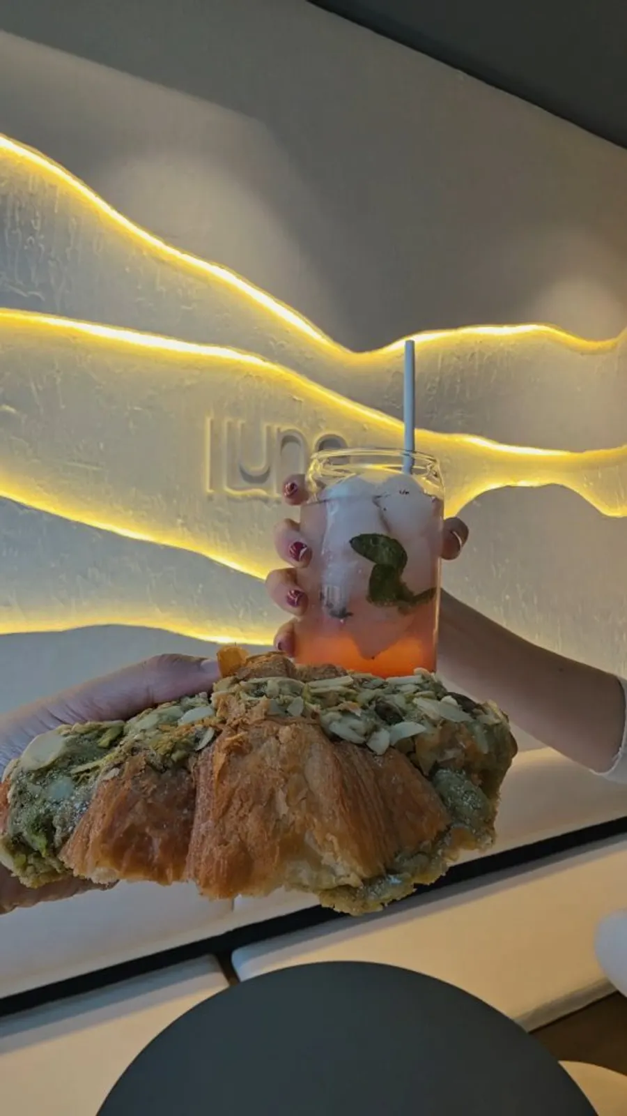 Croissant y bebida fría servidos frente a la pared iluminada de Iluna
